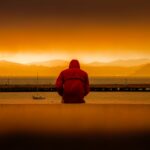 person wearing red hoodie sitting in front of body of water