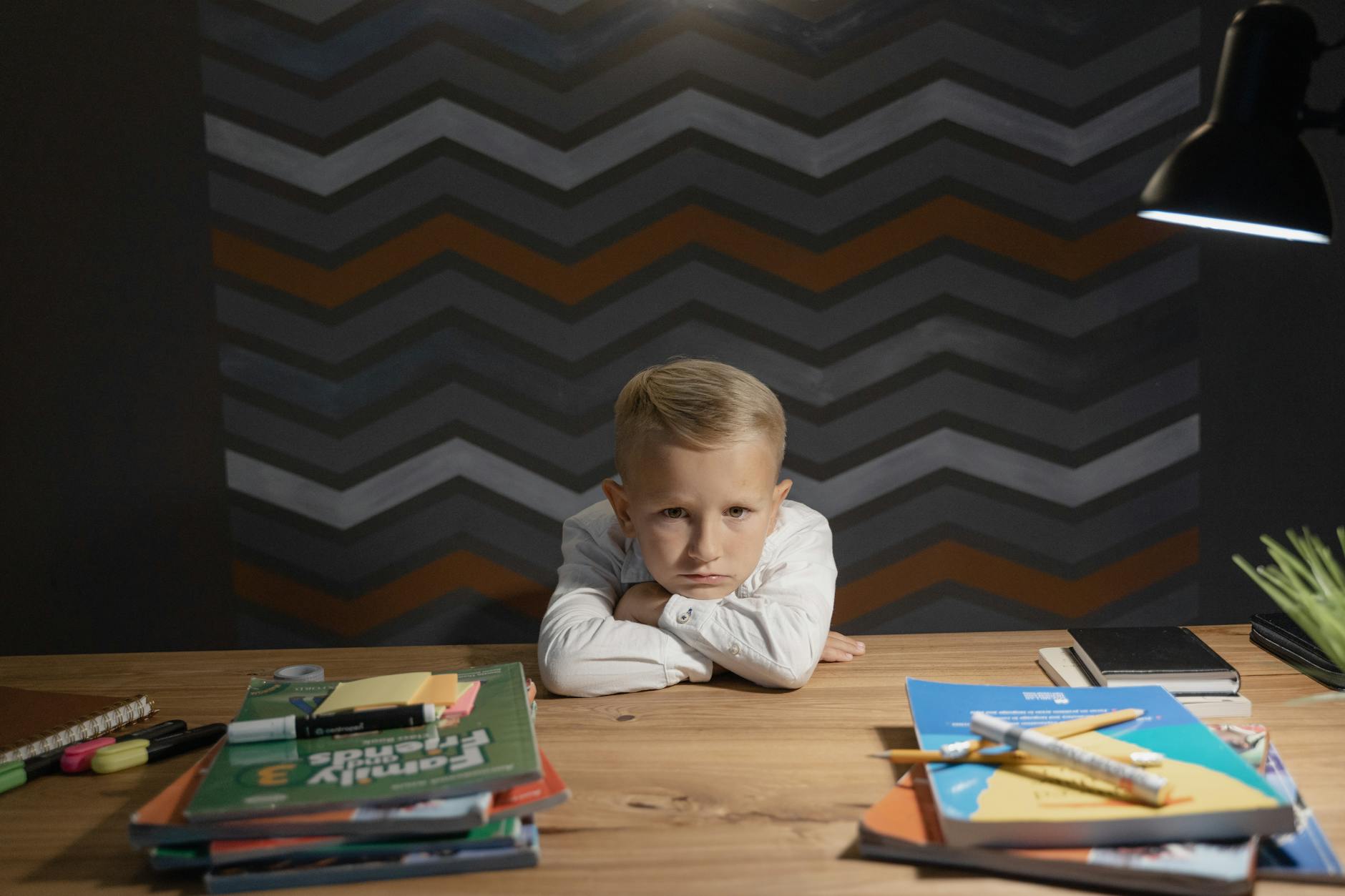 a boy leaning on his crossed arms at a wooden table